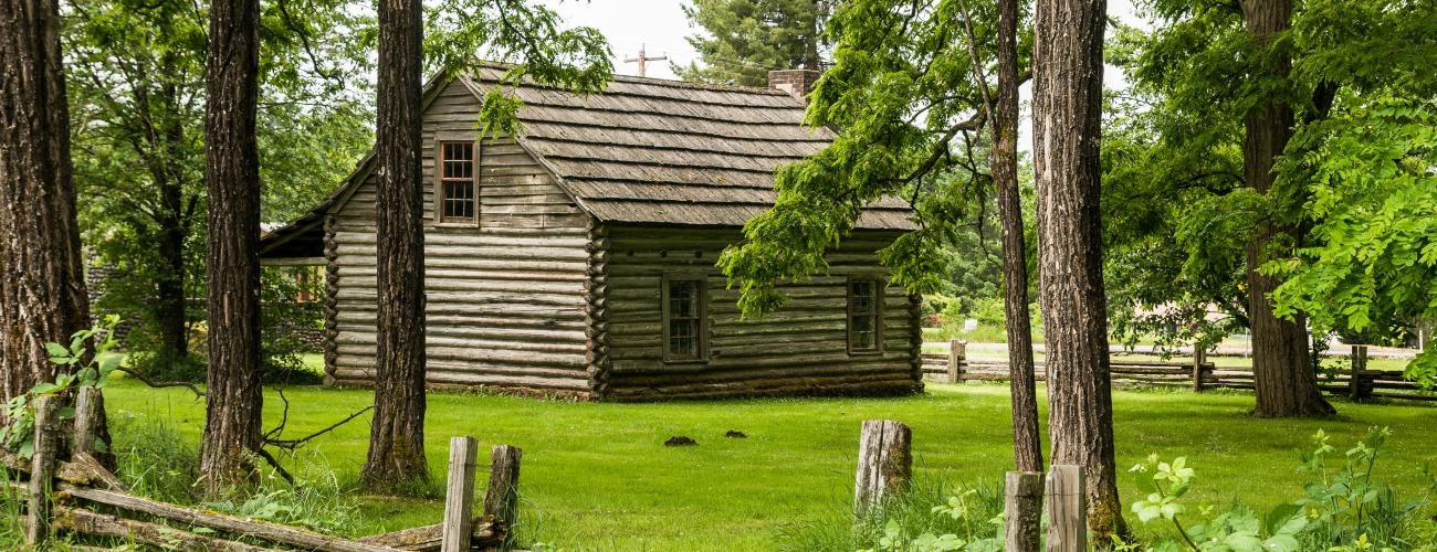 old world cabin of wood surrounded by green grass and wood rail fence