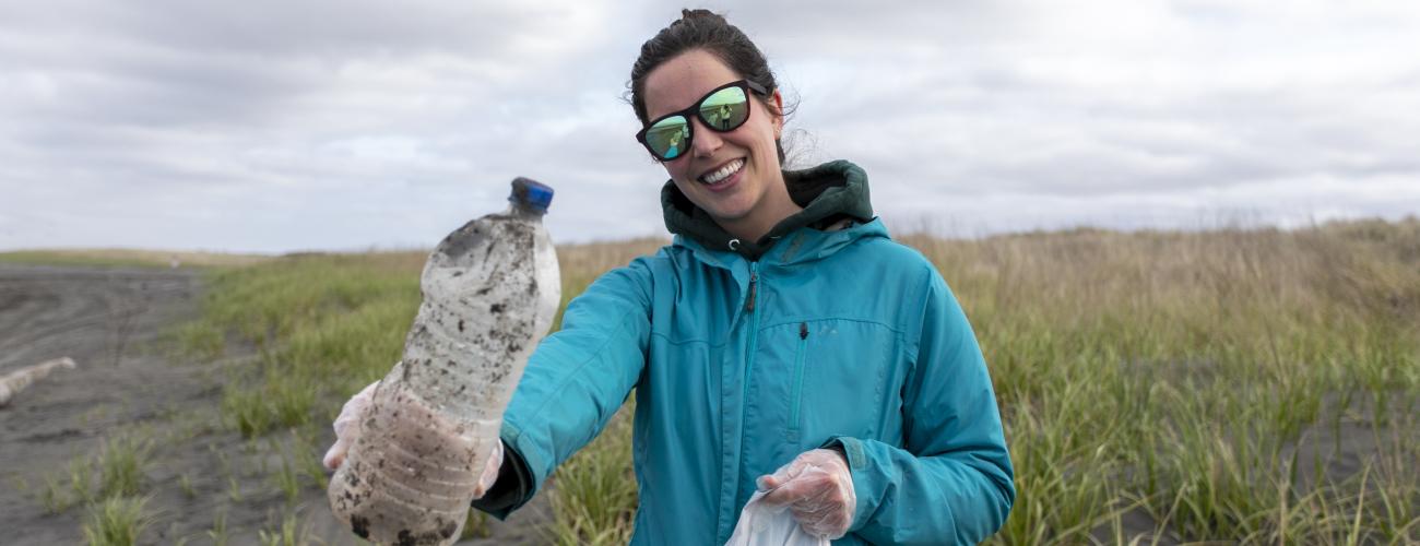 Volunteer in sunglasses collecting trash on a beach.