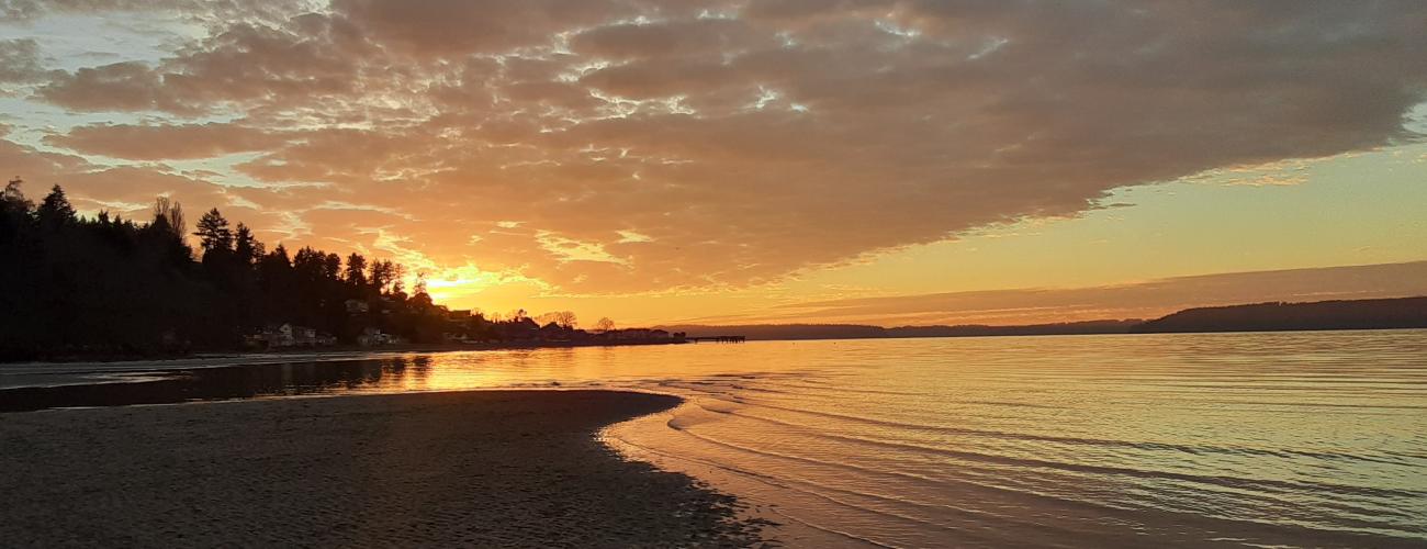 Tide washing over sand, orange sunset with clouds.