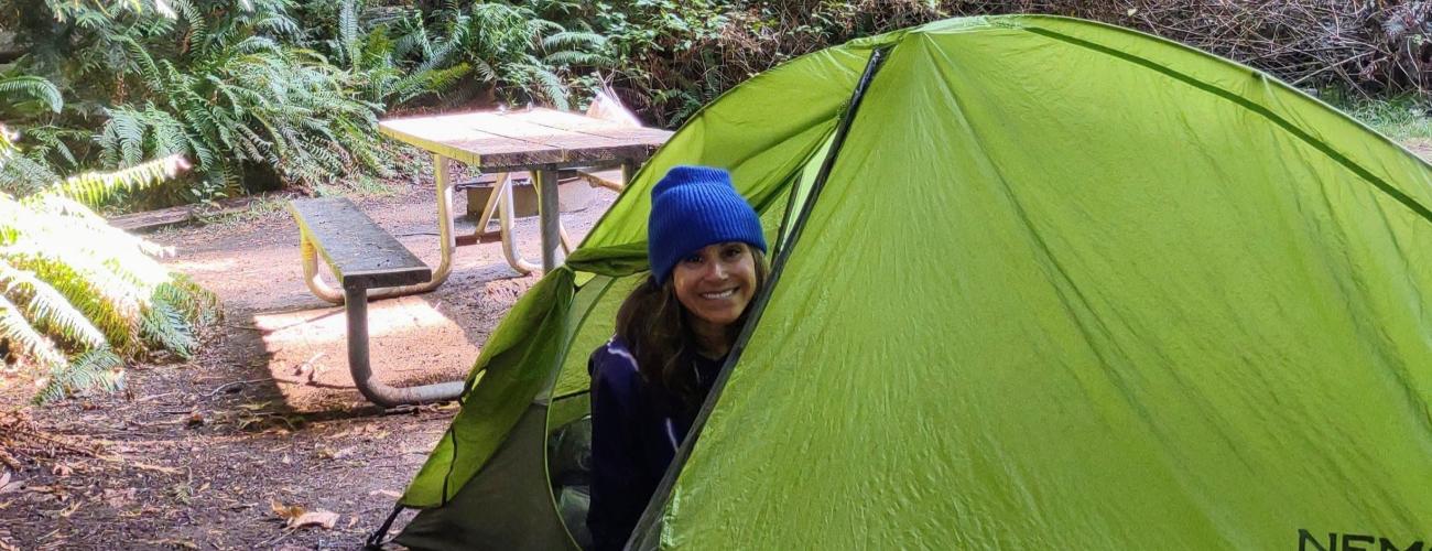 Camper peaks out of a green tent at a camping spot