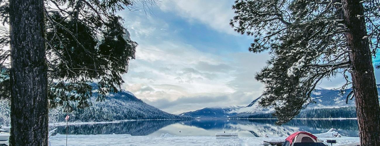 Red tent in a snowy campsite near a lake with mountains in the distance