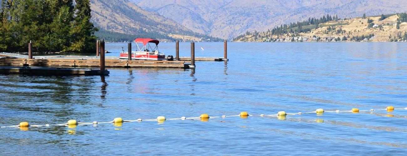 A lake with tan hills in the background and swim area cordoned off in the foreground.