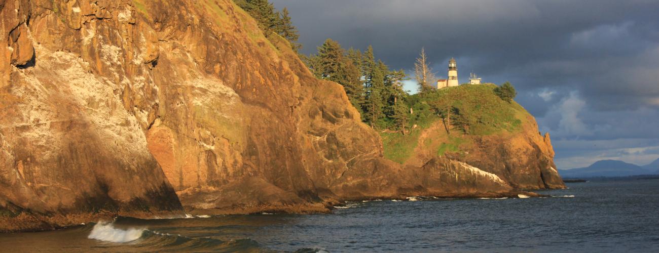 sunlit cliffs with lighthouse above ocean waves