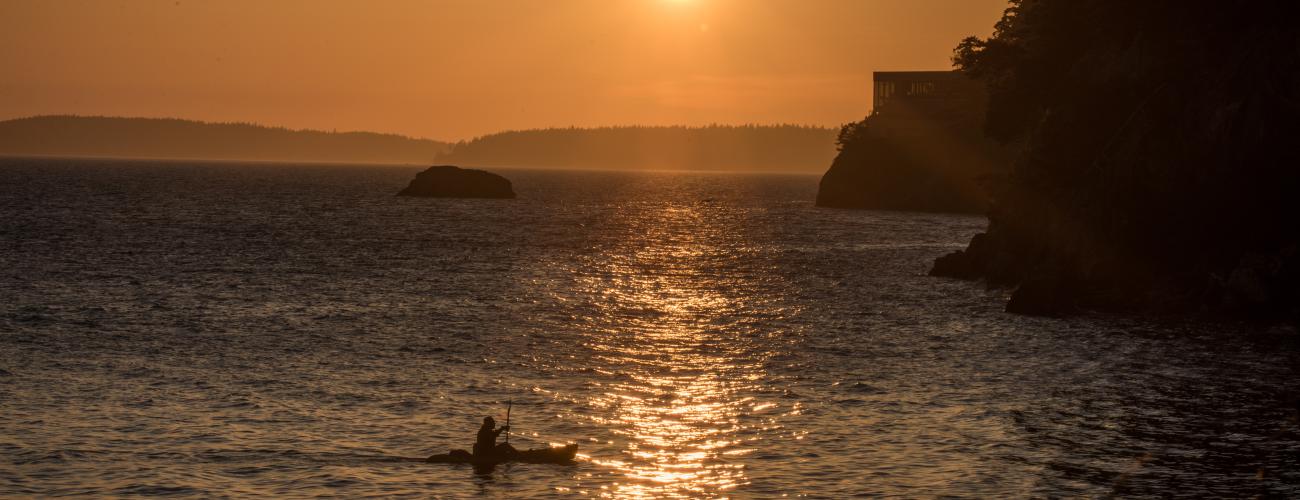 kayaker paddling near shore at sunset