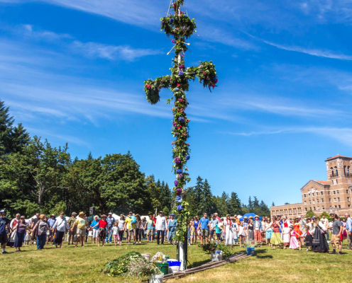 A maypole with onlookers and a brick building in the background