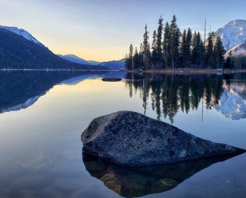 A lake and mountains with rock in foreground at sunrise.