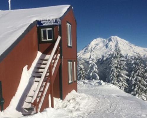 A house with an outside staircase overlooking a mountain and trees in snow