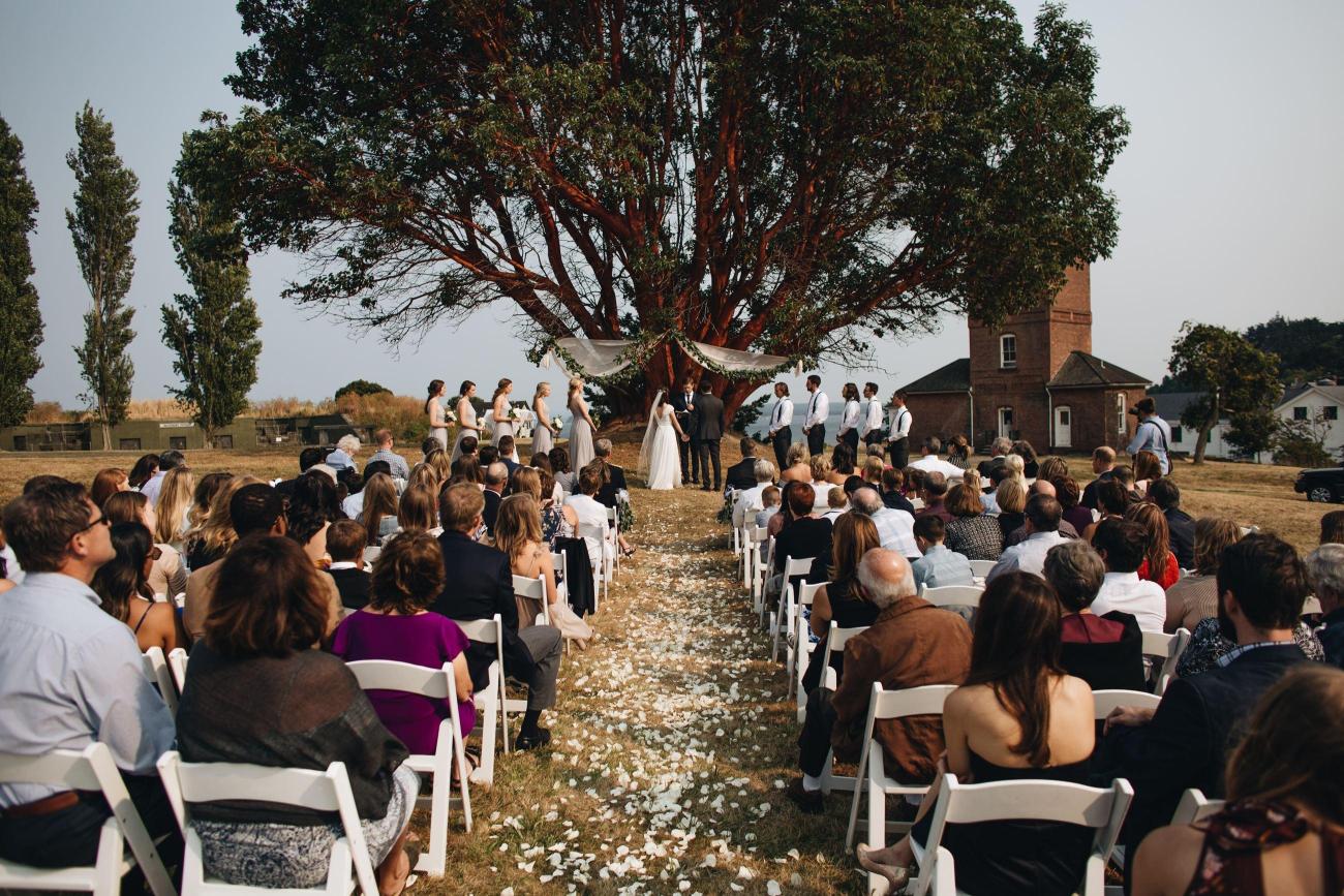 Outdoor wedding at Fort Worden State Park in front of a madrona tree and castle.