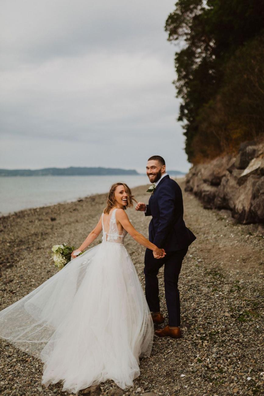 A bride and groom hold hands and run down a beach