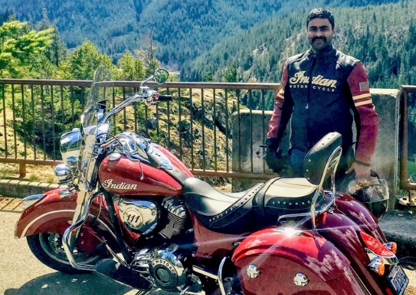 A man stands next to a guard rail with his red motorcycle