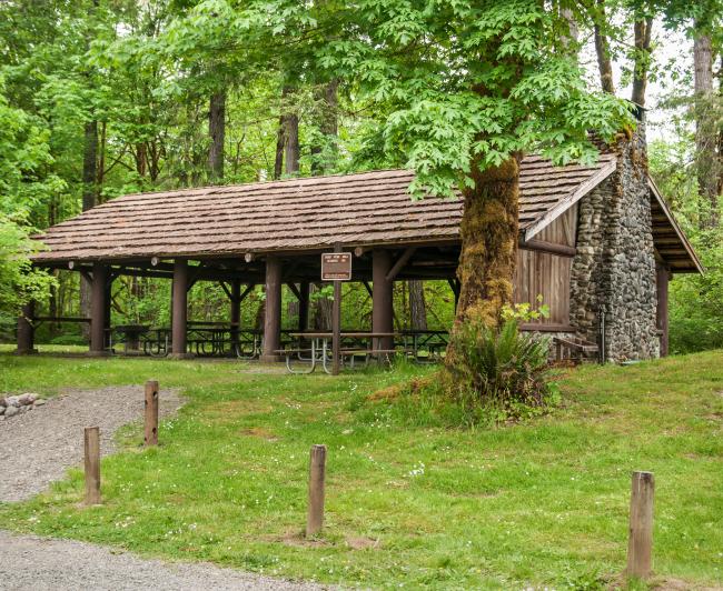 Picnic shelter of stone and wood with forest and green lawn