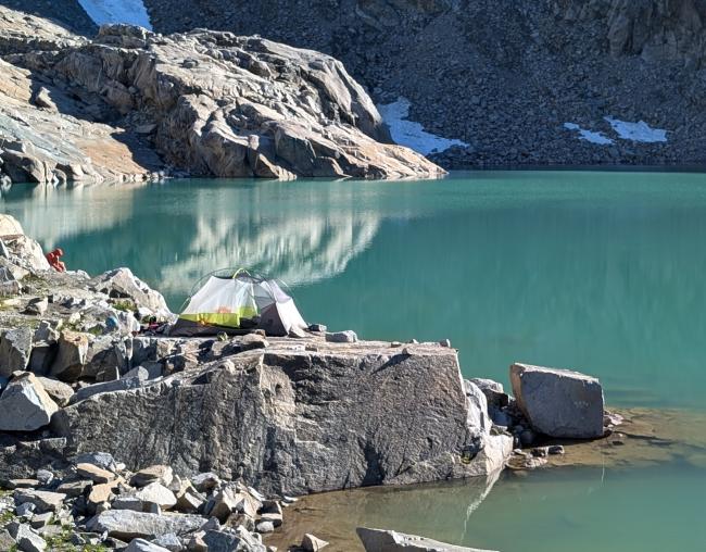 A tent on a rock overlooking a turquoise lake.