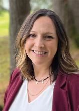 Washington State Parks Administrative Services Director Laura Holmes poses in an evergreen forest wearing a red jacket and white shirt.