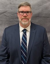 Brian Considine Policy and Governmental Affairs Director wearing, black glasses, a blue suit and tie 