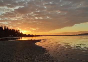 Tide washing over sand, orange sunset with clouds.