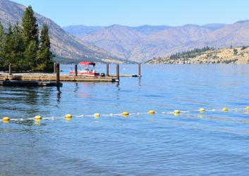 A lake with tan hills in the background and swim area cordoned off in the foreground.