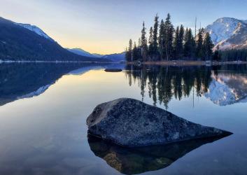 A lake and mountains with rock in foreground at sunrise.