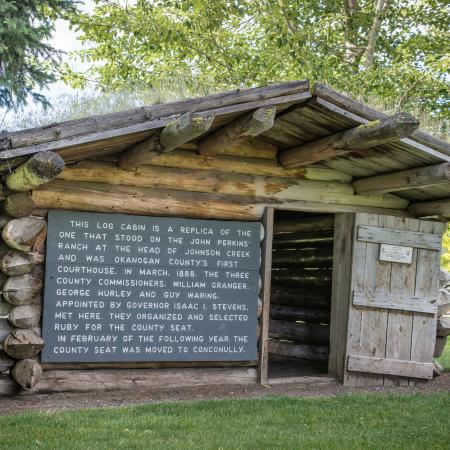 A simple log cabin with the front door open and a large sign on the front.