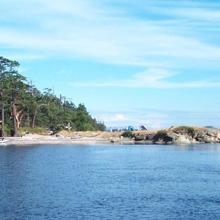 Tents sit on a rocky point with trees, water and a cloudy blue sky around them.