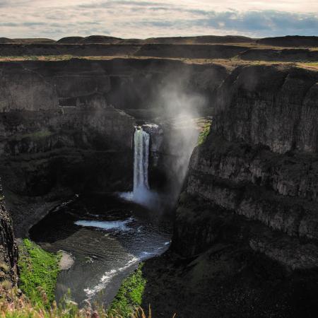 A waterfall at the end of a deep canyon with mist rising from the water below.