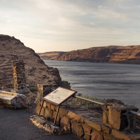 Interpretive panels sit in front of a rock wall with a chain rope with the Columbia River in the background.