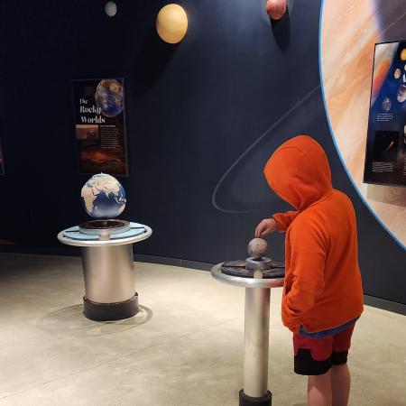 A boy in an orange sweatshirt and red shorts looking at the solar system display in the Goldendale Observatory.