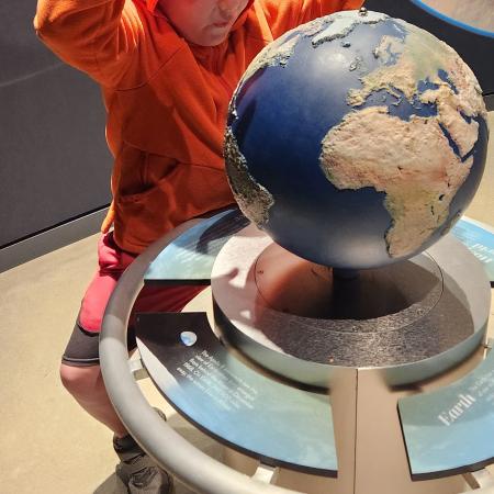 A boy in a orange sweatshirt looking at a globe in the Goldendale Observatory.