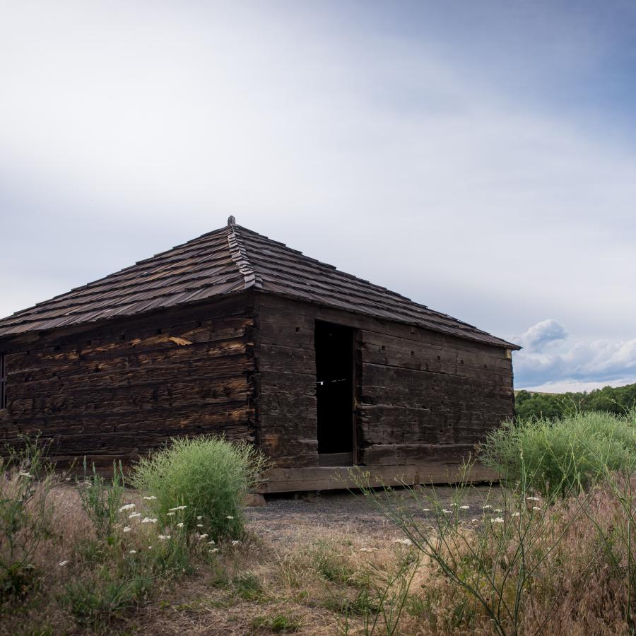 Square style lookout building on top of a hill. Hill in the distance, with a cloudy blue sky.