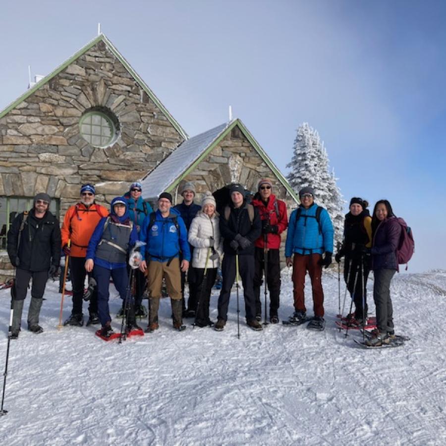 Group of Snowshoers standing in front of a snow covered stone cabin