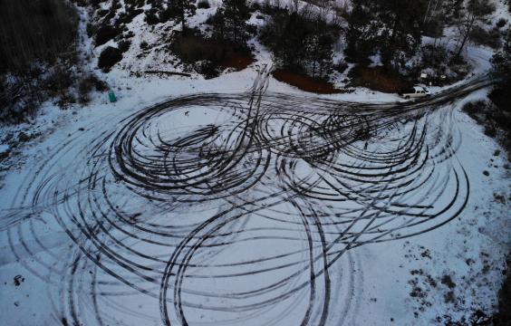 Circular parking area covered by a light layer of snow and looping tire tracks coming off a plowed highway.