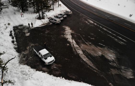 Parking area next to a highway, both plowed clean. A snowy forest lies to the left of the parking area.