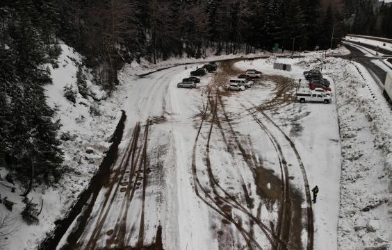 Cars parked in a parking area covered by a thin layer of snow next to a plowed highway. Five porta-potties lie just inside the parking lot entrance.