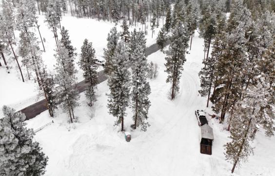 A parking area covered with thick snow next to a plowed highway. A truck with a trailer and a porta-potty sit no the edge of the lot.