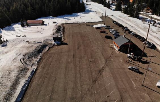 A large, dry, and cleanly plowed parking lot with a small building, next to a sled hill and ski trail with deep snow.