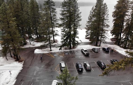 Cleanly plowed paved parking lot with marked parking spots bordered by pines and snowy ground next to a lake. Several trucks are parked in the lot.