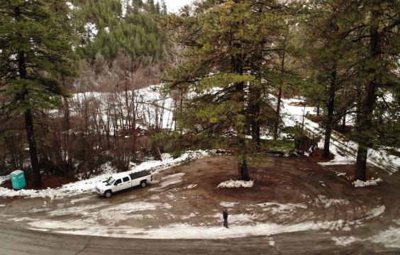 A plowed pull-off parking area with patchy snow next to a forest road. A porta-potty sits on the left side.