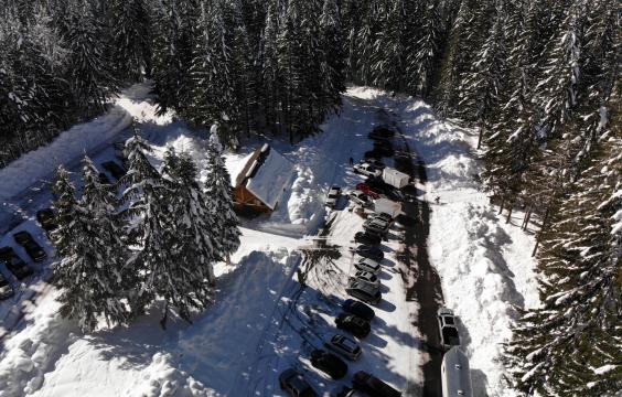 A plowed parking area split by a median with trees and a bathroom facility, surrounded by deep snow and snow-covered trees.