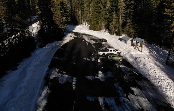 A plowed forest road leading to a plowed parking lot next to a forested  trailhead.