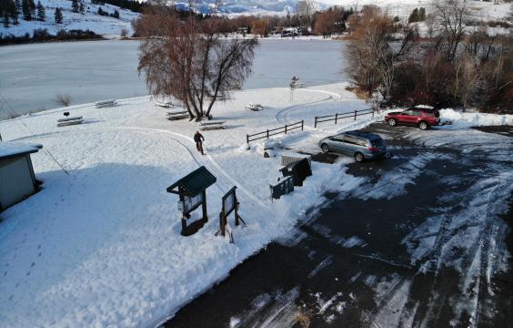 Plowed parking lot next to a snow-covered picnic area, overlooking a frozen lake with snow-covered mountains in the background.